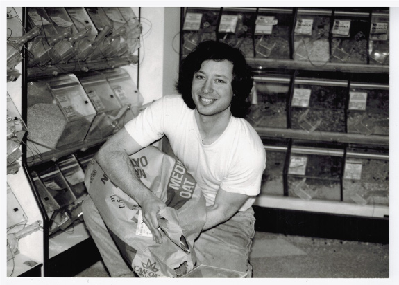 Black and white photo of a smiling young man filling a bulk bin