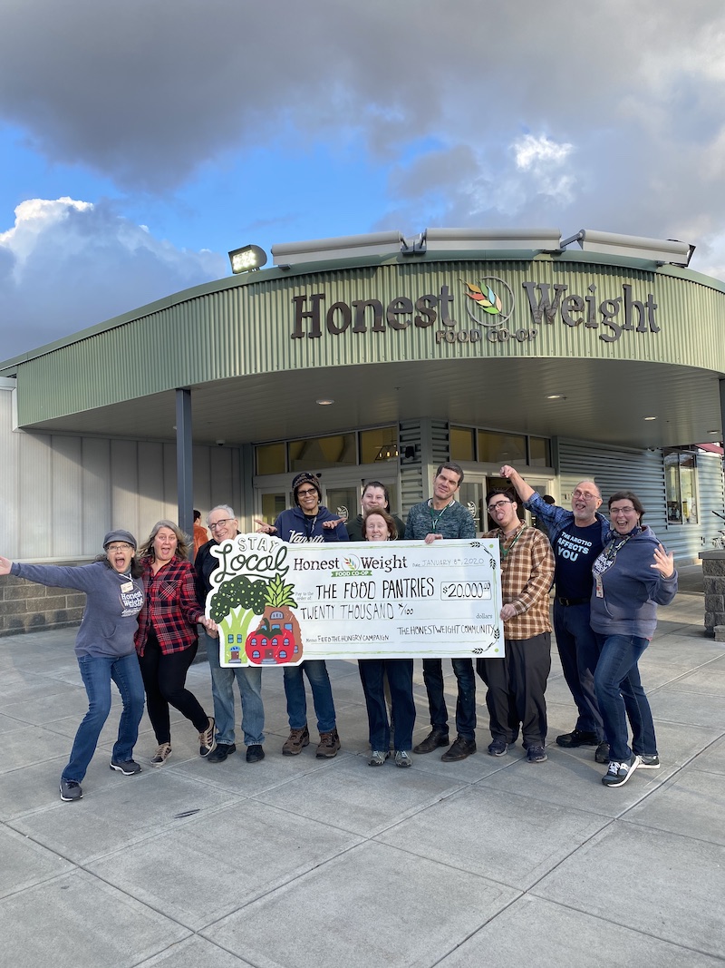 Happy Honest Weight staff standing in front of their store holding a large check for $20,000 made out to The Food Pantries